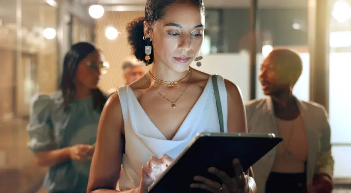 Woman working on her ipad in the office with 2 women talking behind her